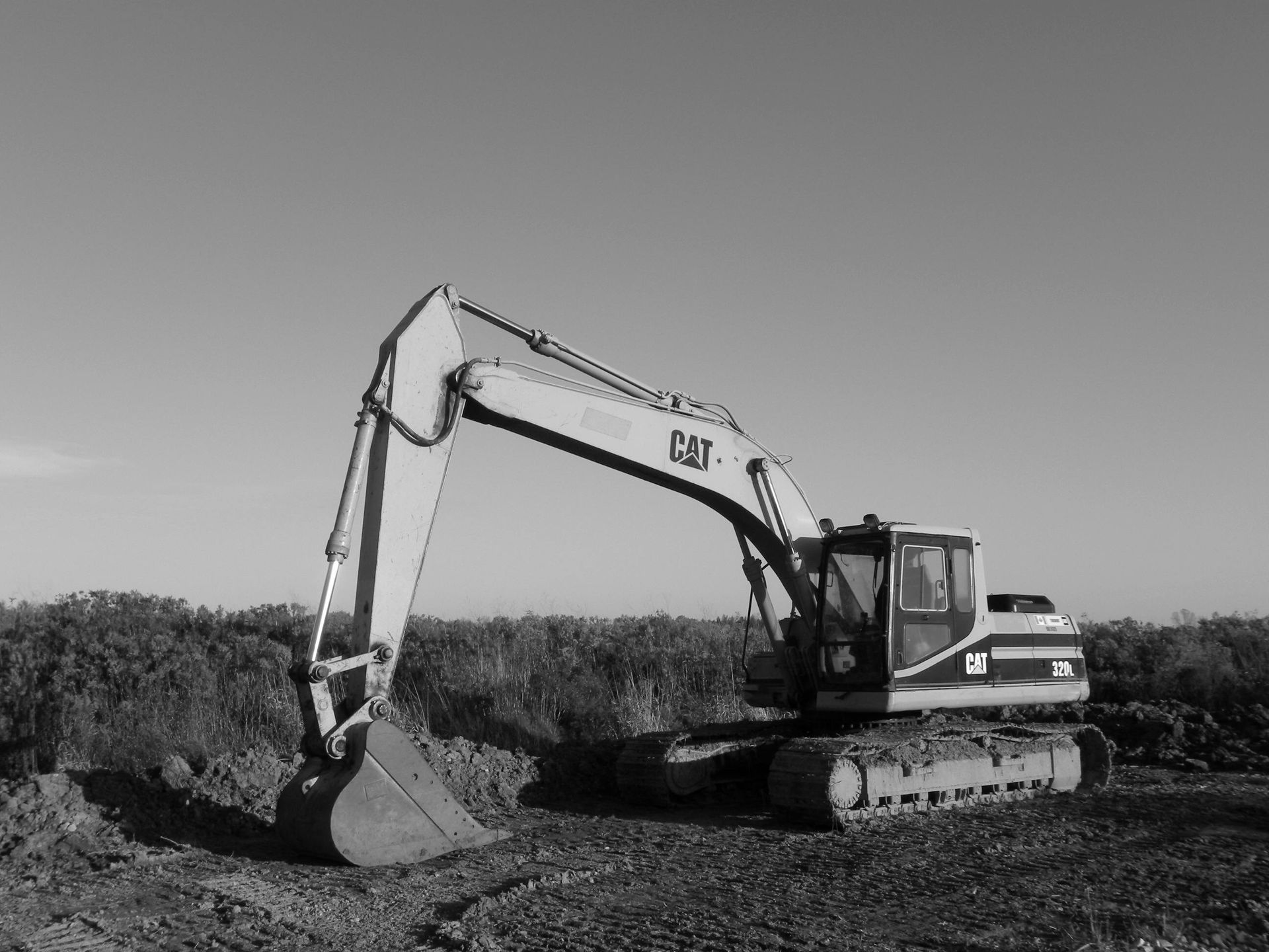 White excavator digging in a dirt field under a clear sky.