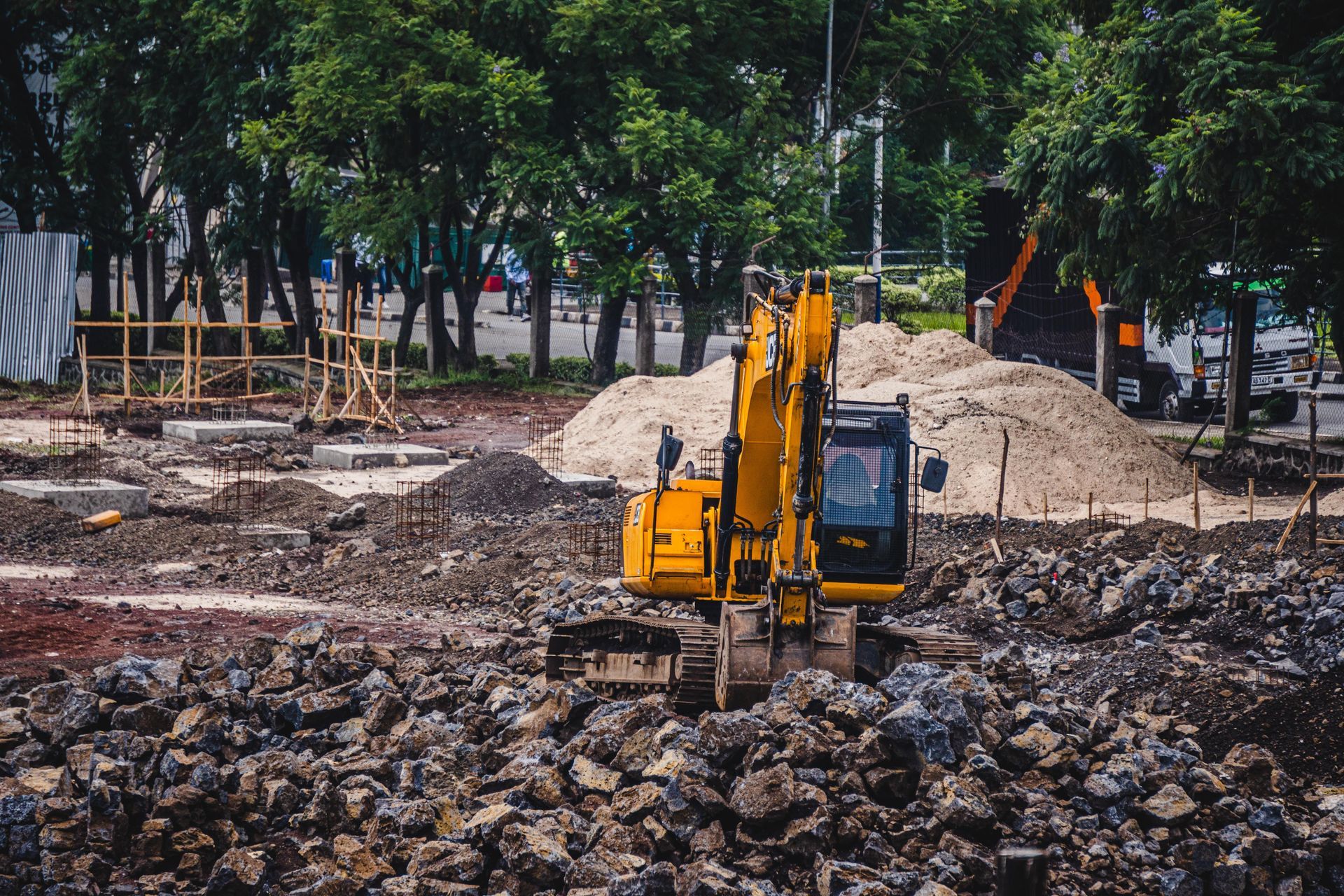Yellow excavator working on a rocky construction site with dirt piles and trees in the background