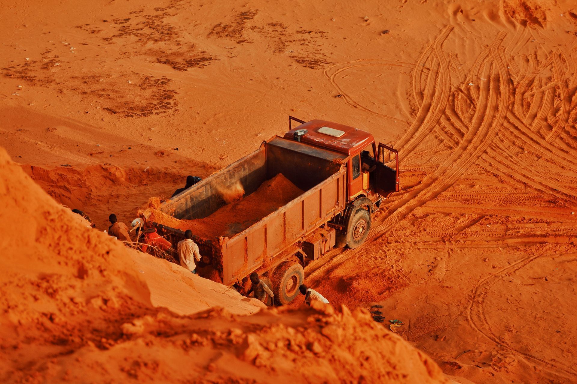 Orange dump truck hauling dirt on a red sandy slope at a construction site