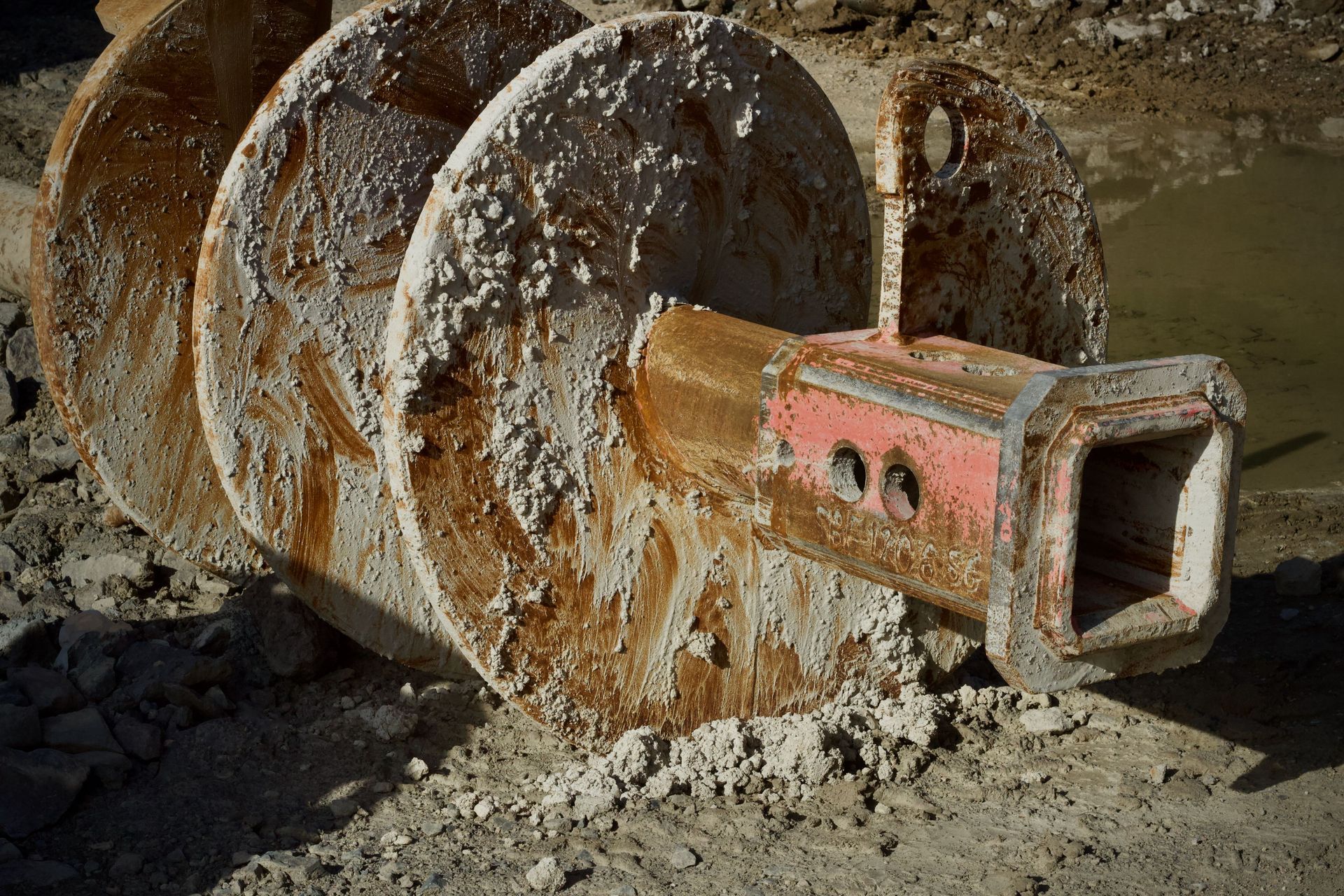 Rusty excavator bucket covered in dried mud, resting on dirt.