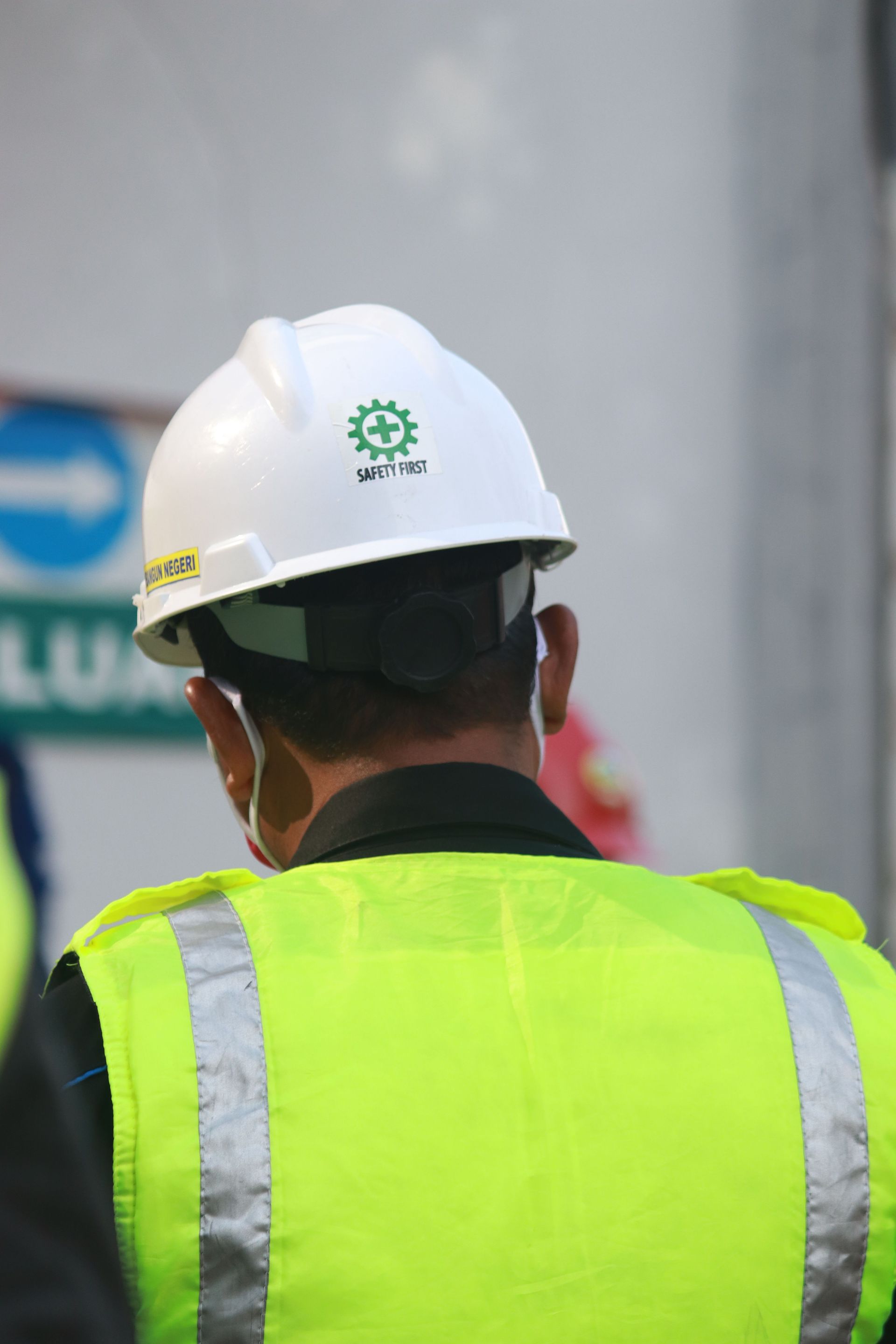 Worker in a white hard hat and neon yellow safety vest seen from behind at a construction site.