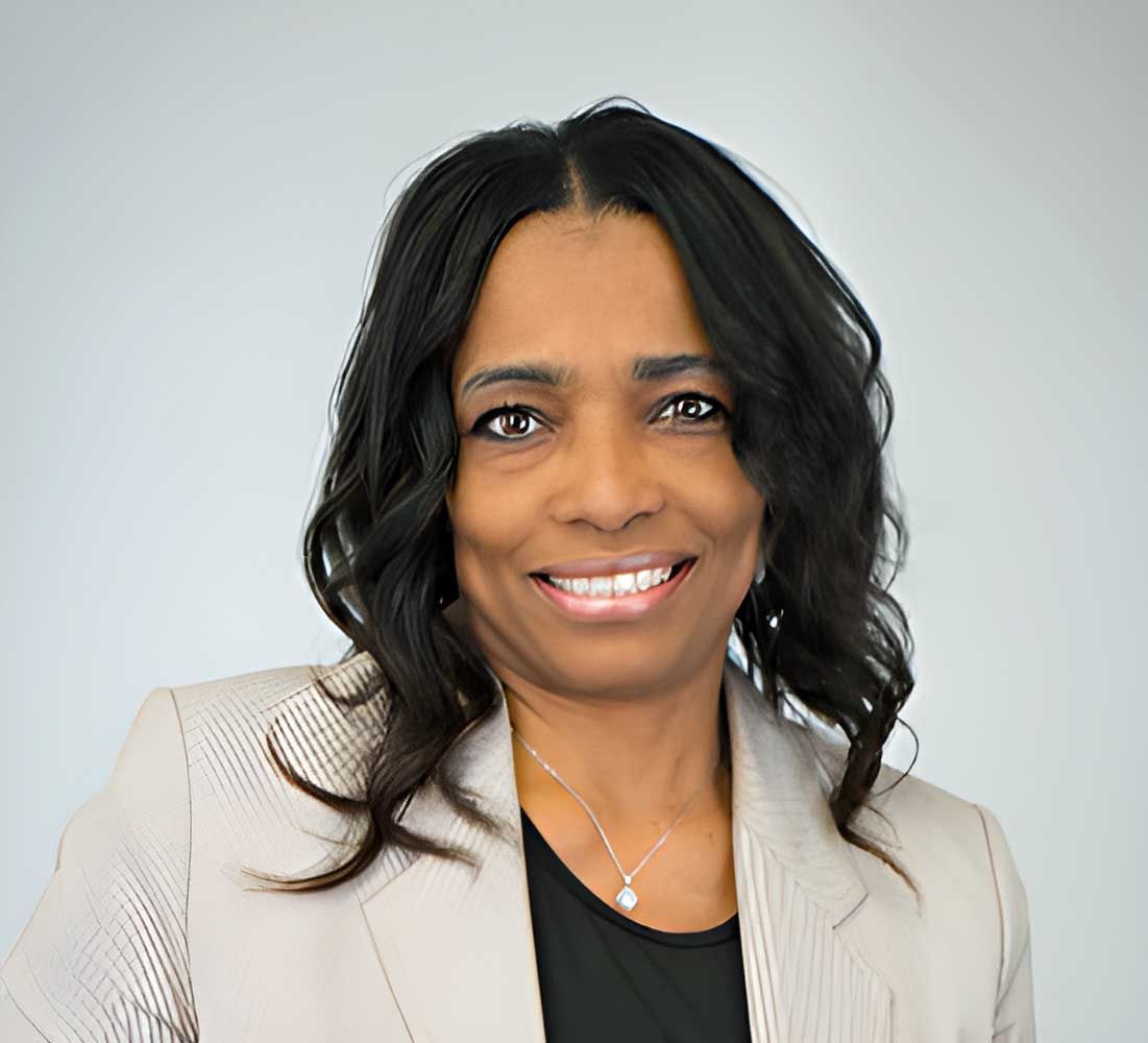 Lisa Williams smiles, wearing a cream blazer and black top. White background.