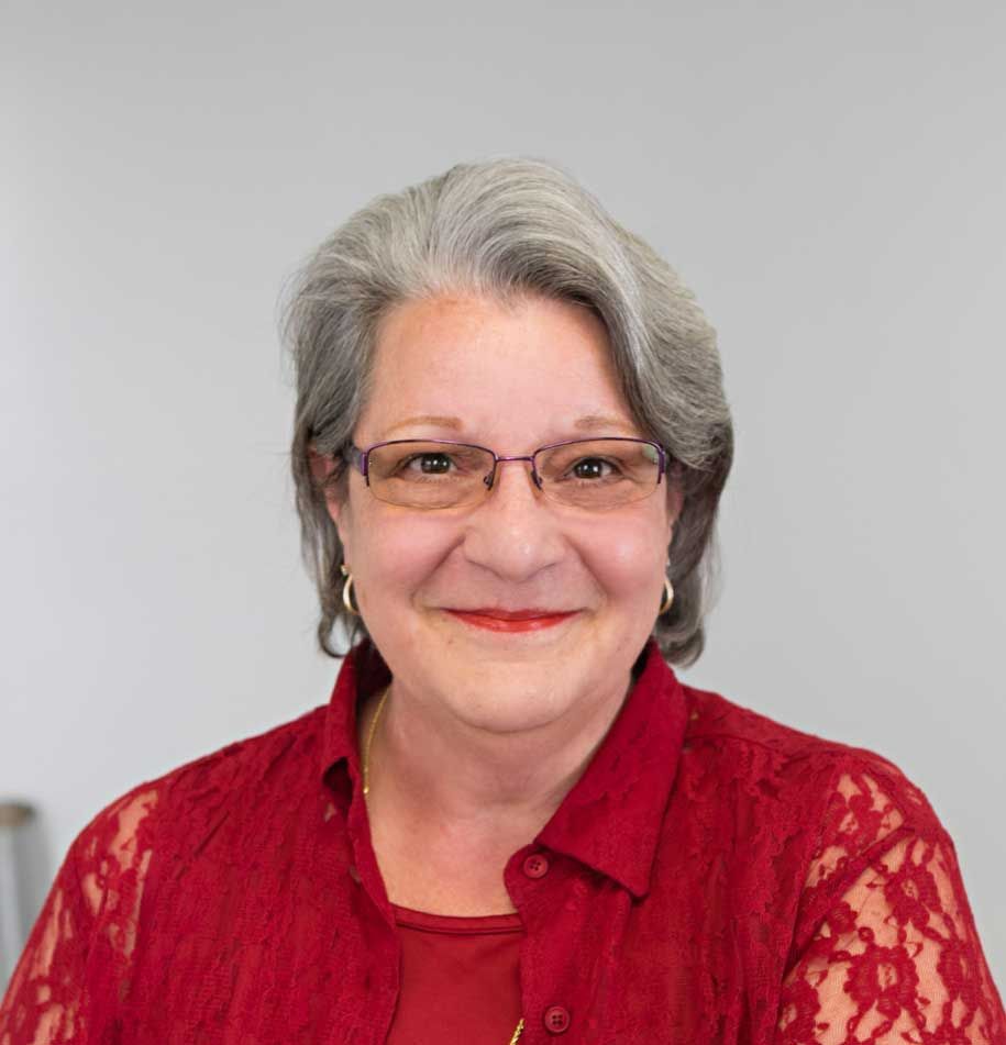 Michele Muller with glasses wearing a red lace top, smiling at the camera.