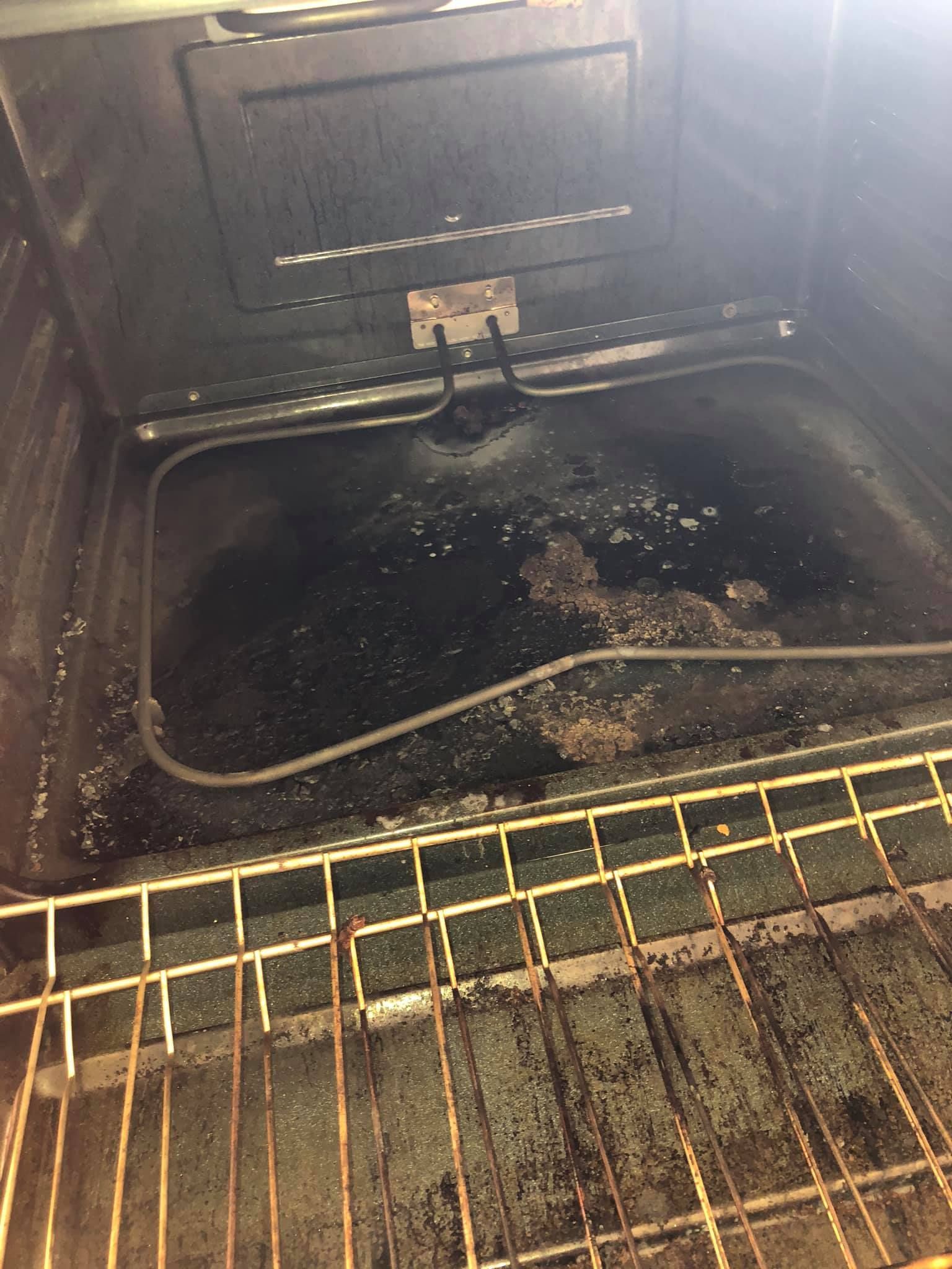 The interior of an oven with a dirty, grease-stained floor and a dark heating element, viewed from the front.