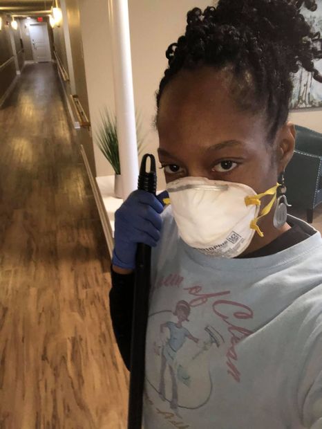A person wearing a face mask and blue gloves holding a cleaning tool in a long hallway.