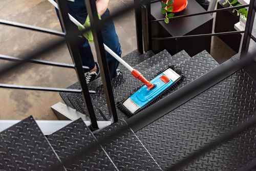 A person in blue pants cleans metal stairs with a blue and white mop.