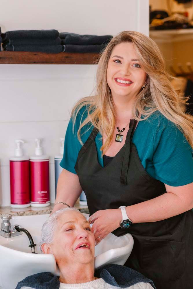 A woman is washing another woman 's hair in a sink in a salon.