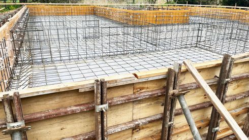Concrete foundation formwork with steel rebar mesh and wooden supports at a construction site