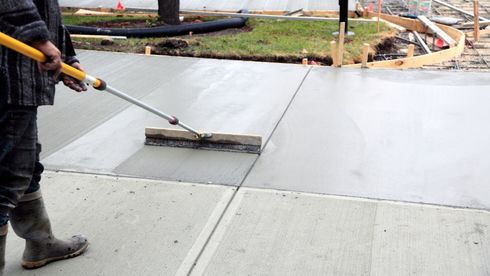 Worker smoothing wet concrete on a driveway with a long-handled screed