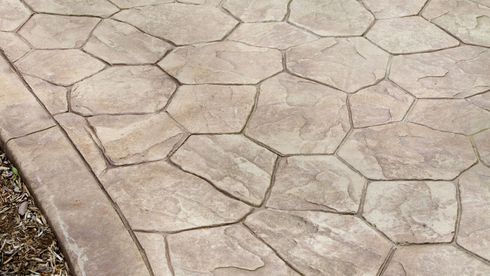 Stamped concrete walkway with beige stone pattern and a curb along the left edge