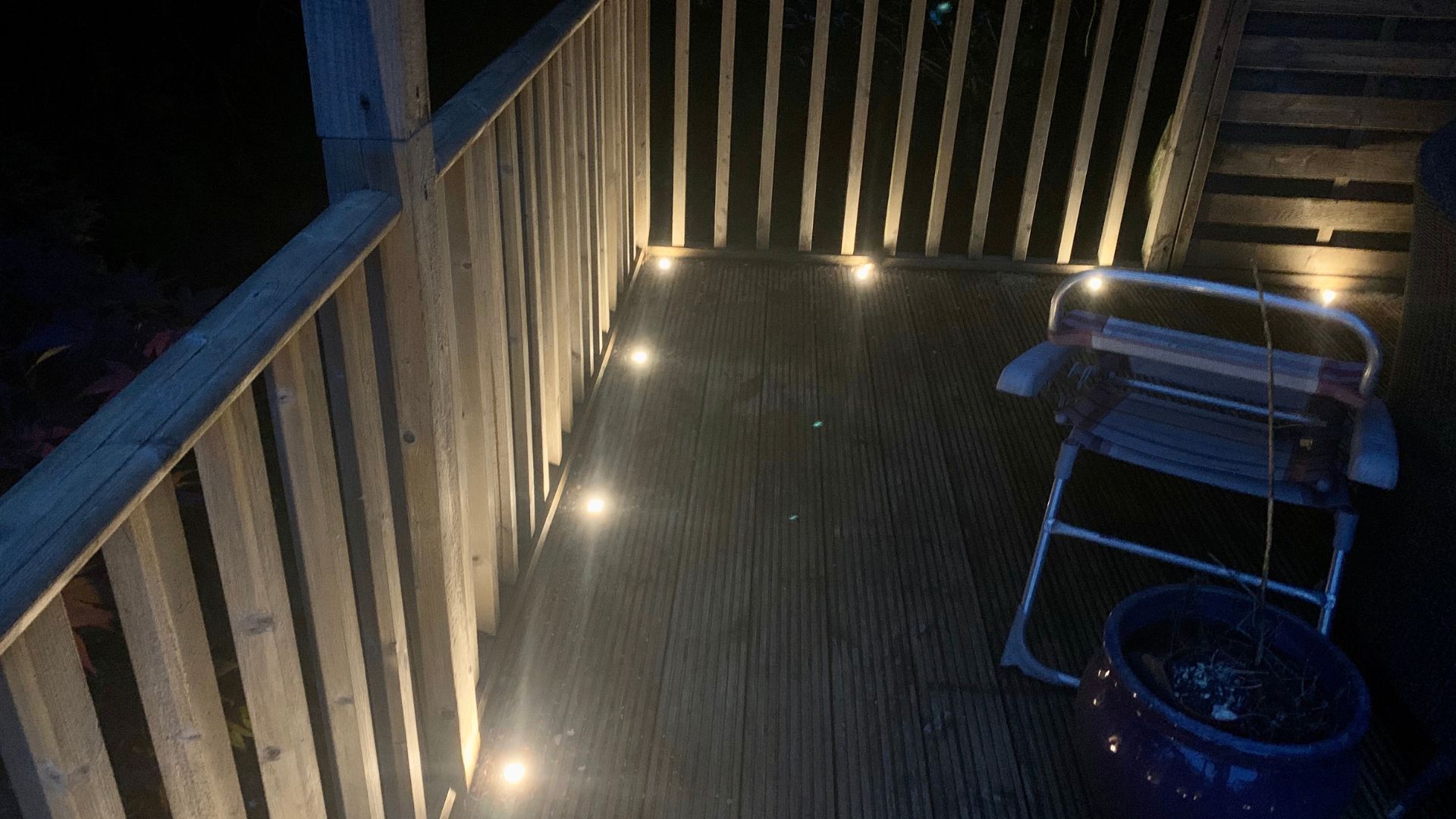 Deck at dusk with railing lights, a grill, and a blue bucket on the floor.