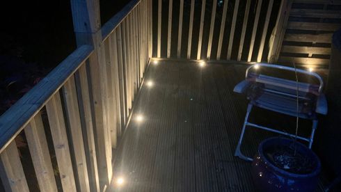 Deck at night with railing lights, a grill, and a blue planter.