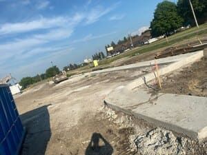 Roadside construction site with concrete curbs, dirt lot, and blue fencing under a clear sky