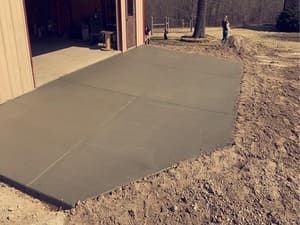 Fresh concrete driveway apron beside a tan garage in a wooded yard
