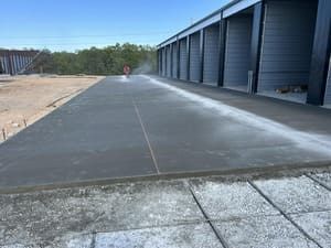 Wide concrete walkway beside blue industrial buildings and dirt lot on a clear day