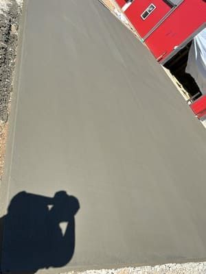 Gray pavement beside a red building, with a person’s shadow in the lower left corner