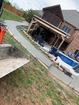 Tilted view of a brick house with a backyard pool, patio, and lawn on a sloped yard