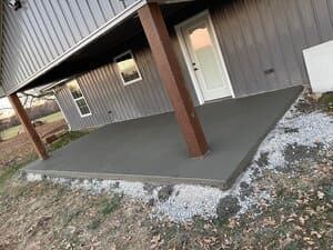 Concrete porch ramp beside a metal-sided building with brown support posts and a white door
