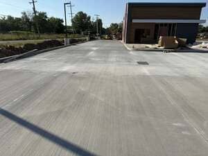 New concrete driveway beside a building, with construction materials and utility poles in the background