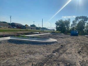 Empty dirt lot with concrete drainage basins, blue dumpster, and bright sky with sun flare