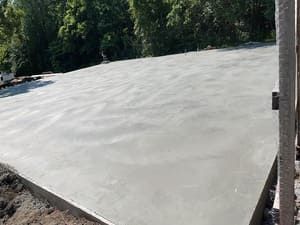 Freshly poured concrete slab beside a wooded area, viewed from an angle
