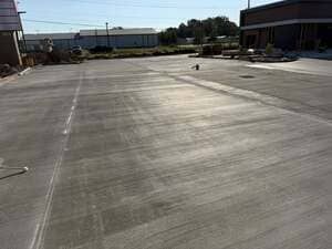 Wide concrete parking lot under bright sun with a few buildings in the background.