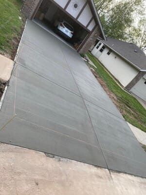 Concrete driveway leading to a garage with a parked car, viewed at an angle in a suburban neighborhood.