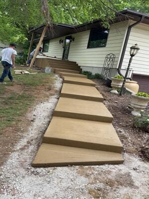 New concrete steps leading up a sloped path beside a white house; person walking nearby