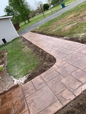 Curved stamped concrete walkway beside a lawn and house, extending toward a street