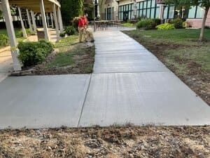 Concrete sidewalk path leading to a building entrance beside landscaped grass and bushes