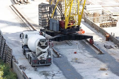 Construction site with a white concrete mixer truck beside a yellow crane on a snowy ground