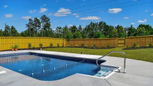 Backyard swimming pool with blue water, concrete deck, and a wooden fence under a sunny sky
