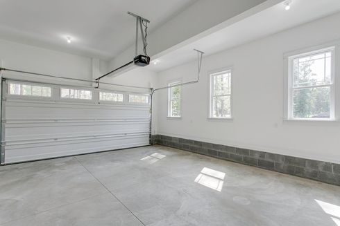 Empty white garage with concrete floor, windows, and a closed roll-up door.