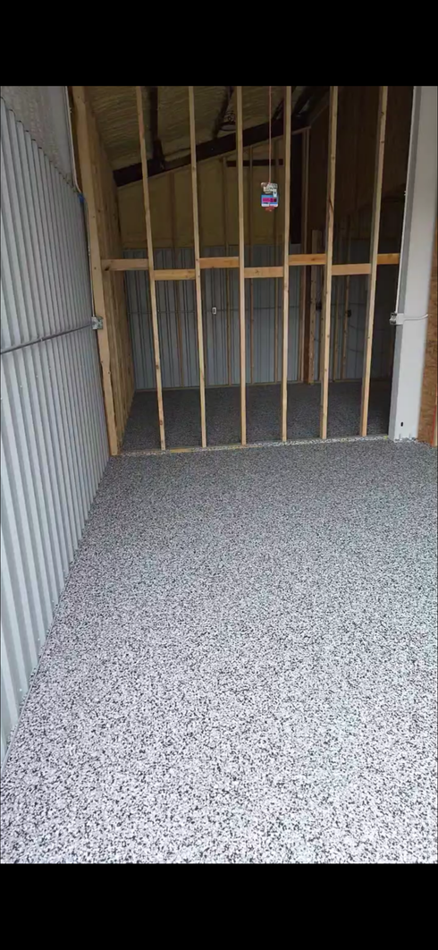 Empty hallway with exposed wooden studs and a speckled carpet floor, leading to a closed door.