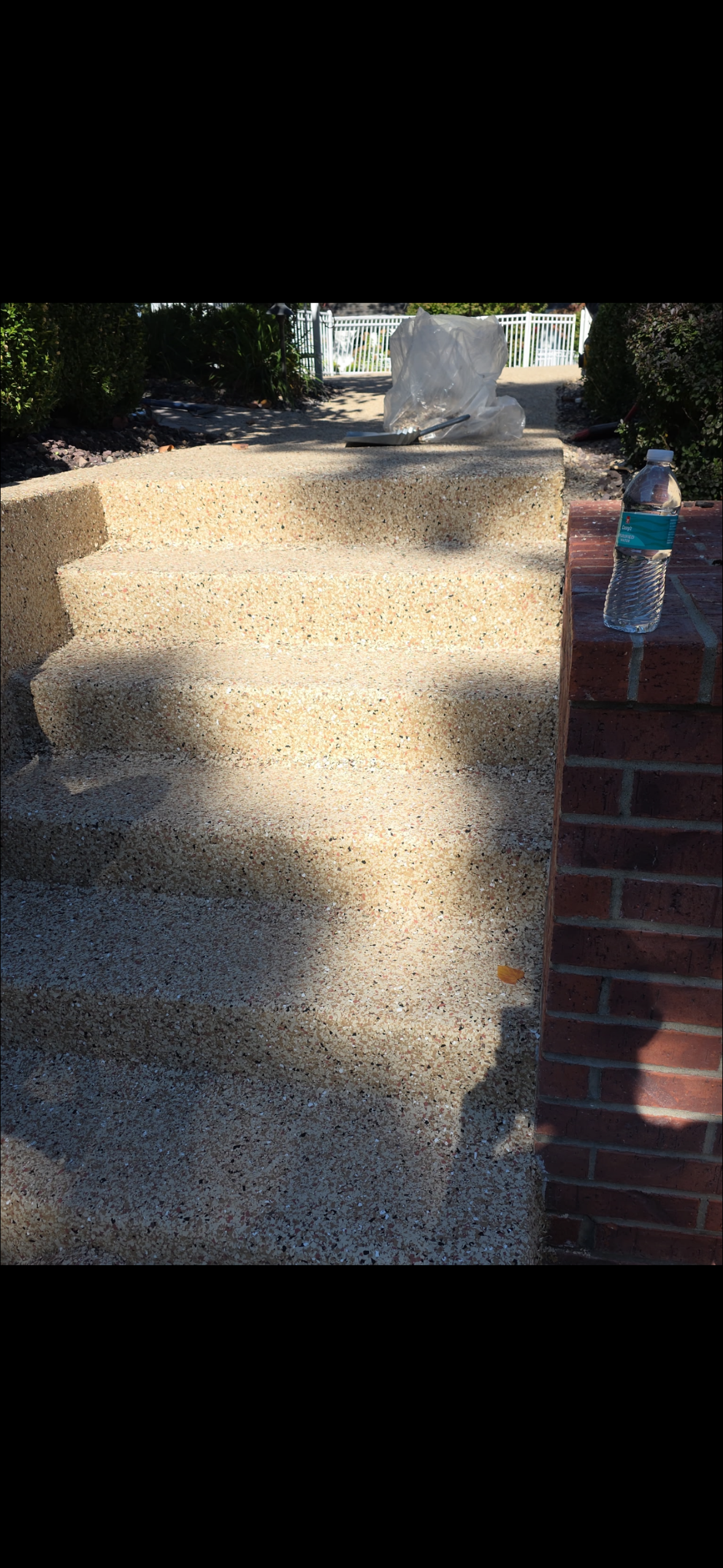 Gravel driveway beside a brick wall, with sunlight and tree shadows across the path