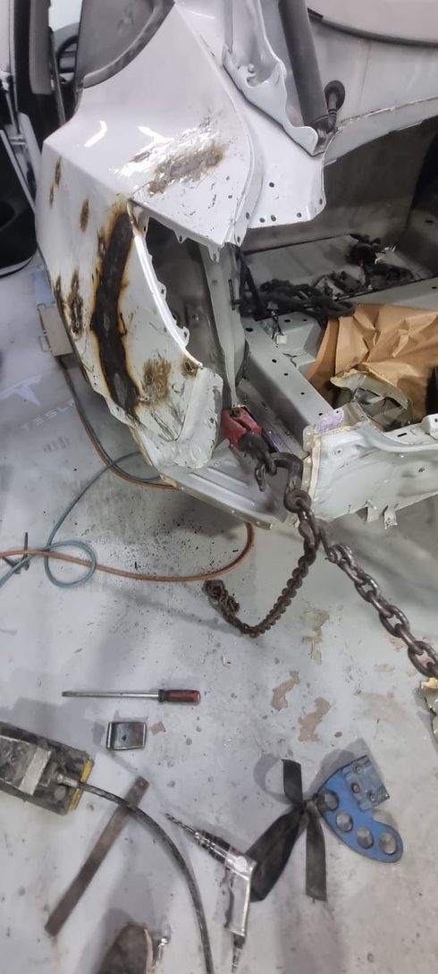 Damaged car body in a repair shop with tools and chains.