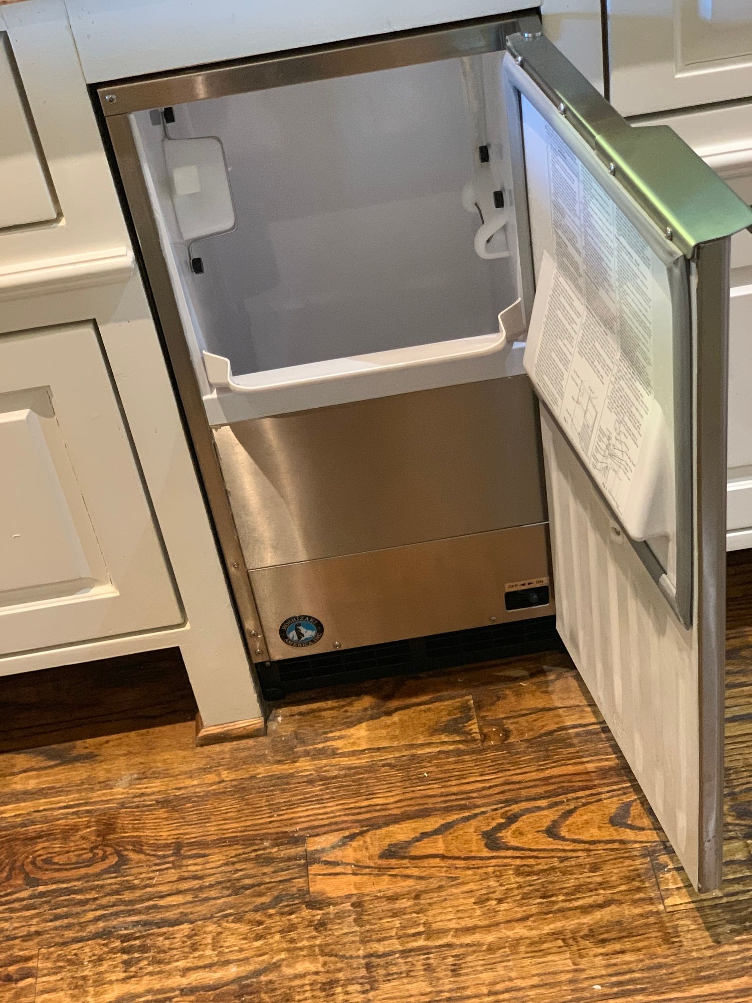 a stainless steel ice maker is sitting on a wooden floor in a kitchen .