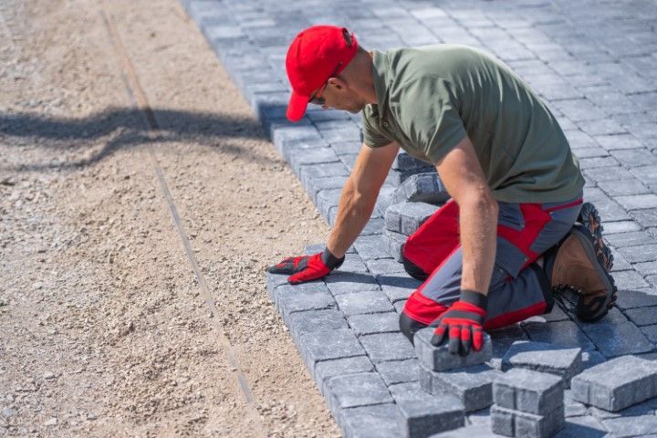 Worker in red cap laying gray pavers on a driveway under construction