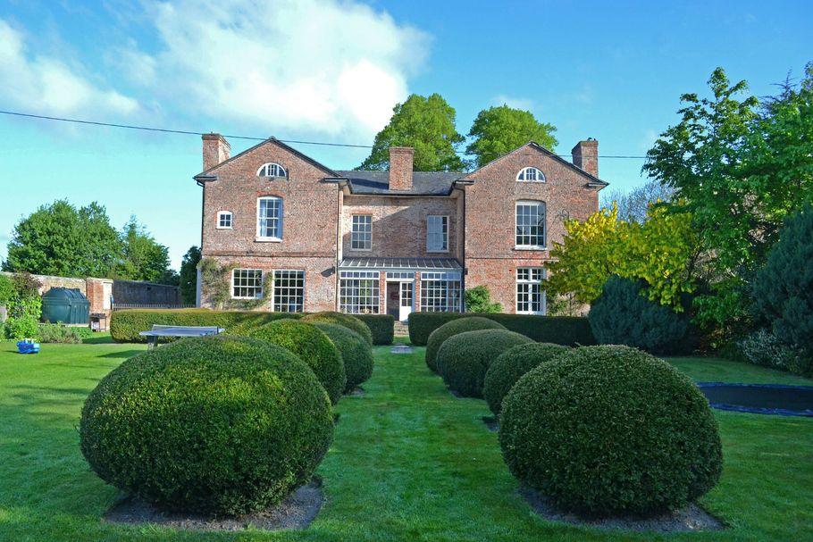 Brick manor house with manicured lawn, rounded hedges, and blue sky