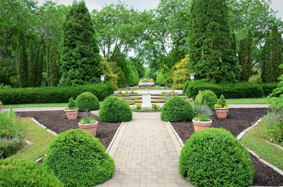 Formal garden with trimmed hedges, stone path, and central fountain surrounded by lush greenery