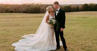 Bride and groom embracing in a field at sunset, bride in a long white veil and dress, groom in black suit