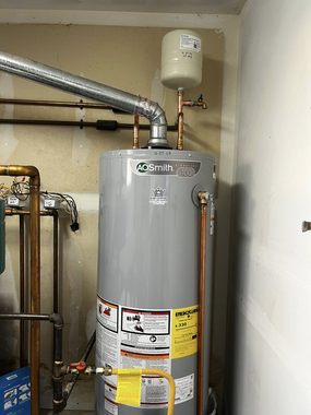 A grey residential water heater with a connected exhaust vent and expansion tank in a basement setting.