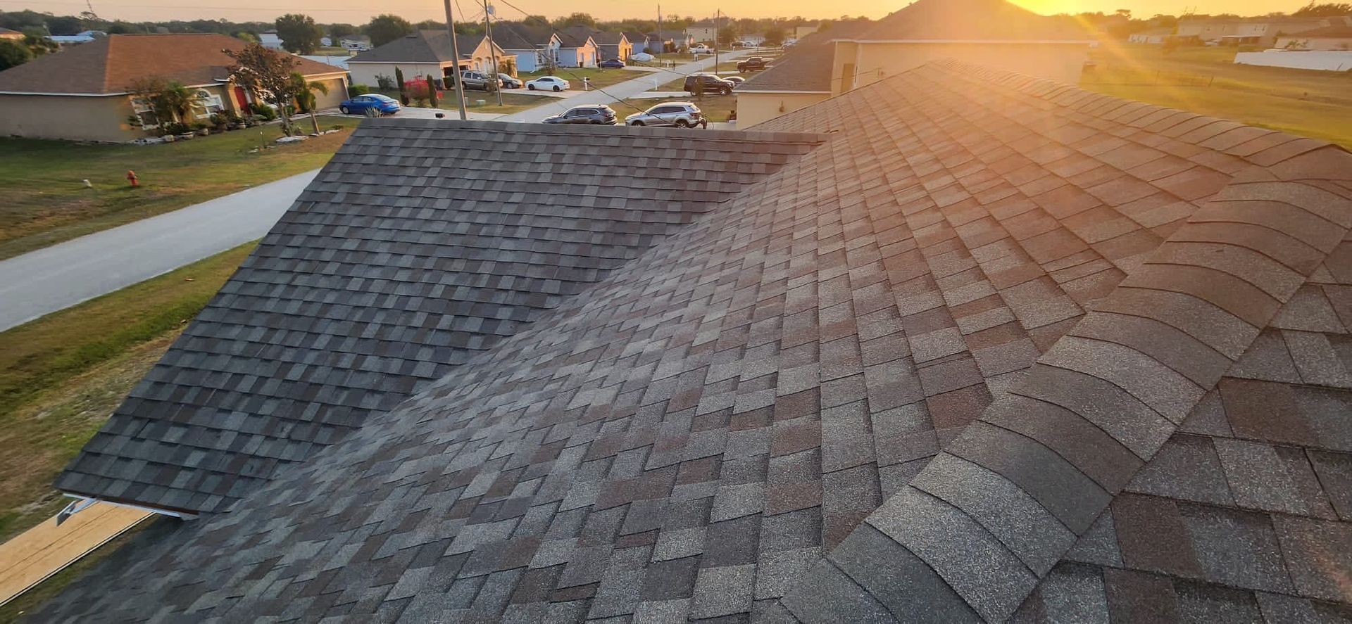 Sunlit gray shingle roof with neighborhood houses in the distance at sunset