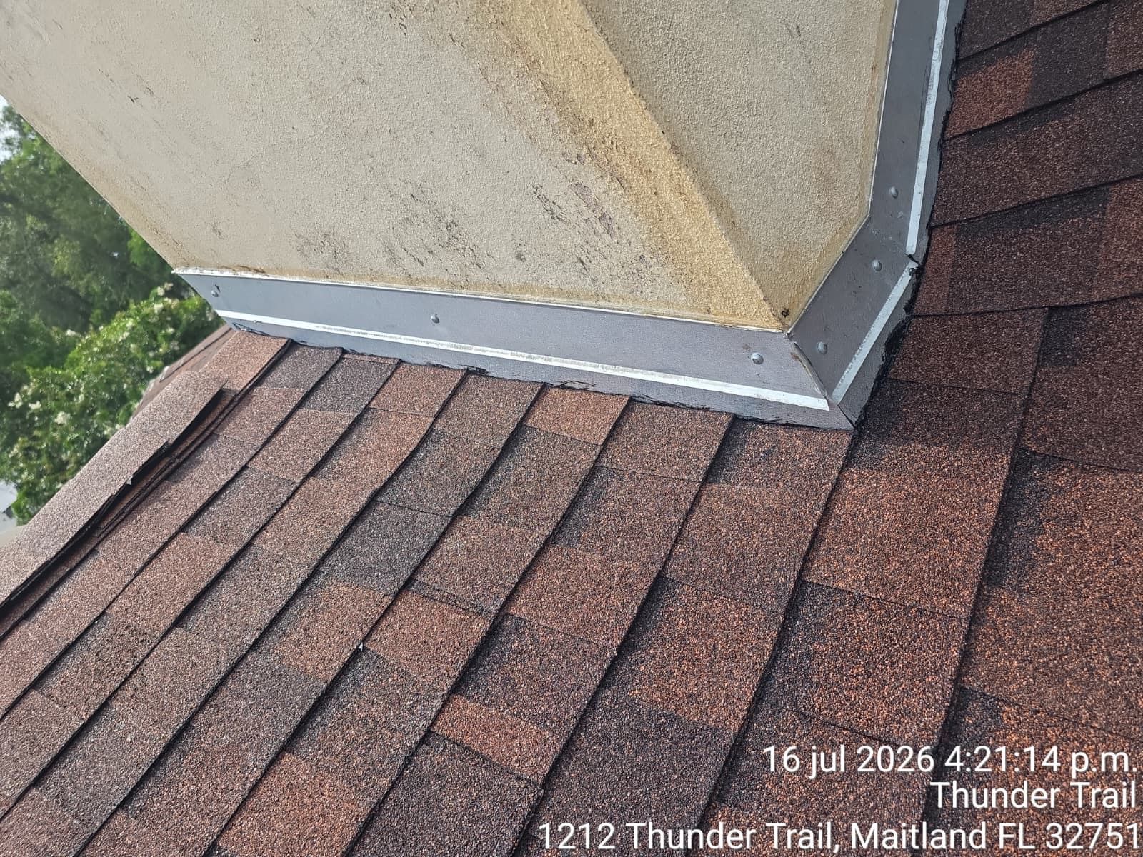 Roof shingles meeting stucco chimney flashing at a roof corner, with worn caulk visible.