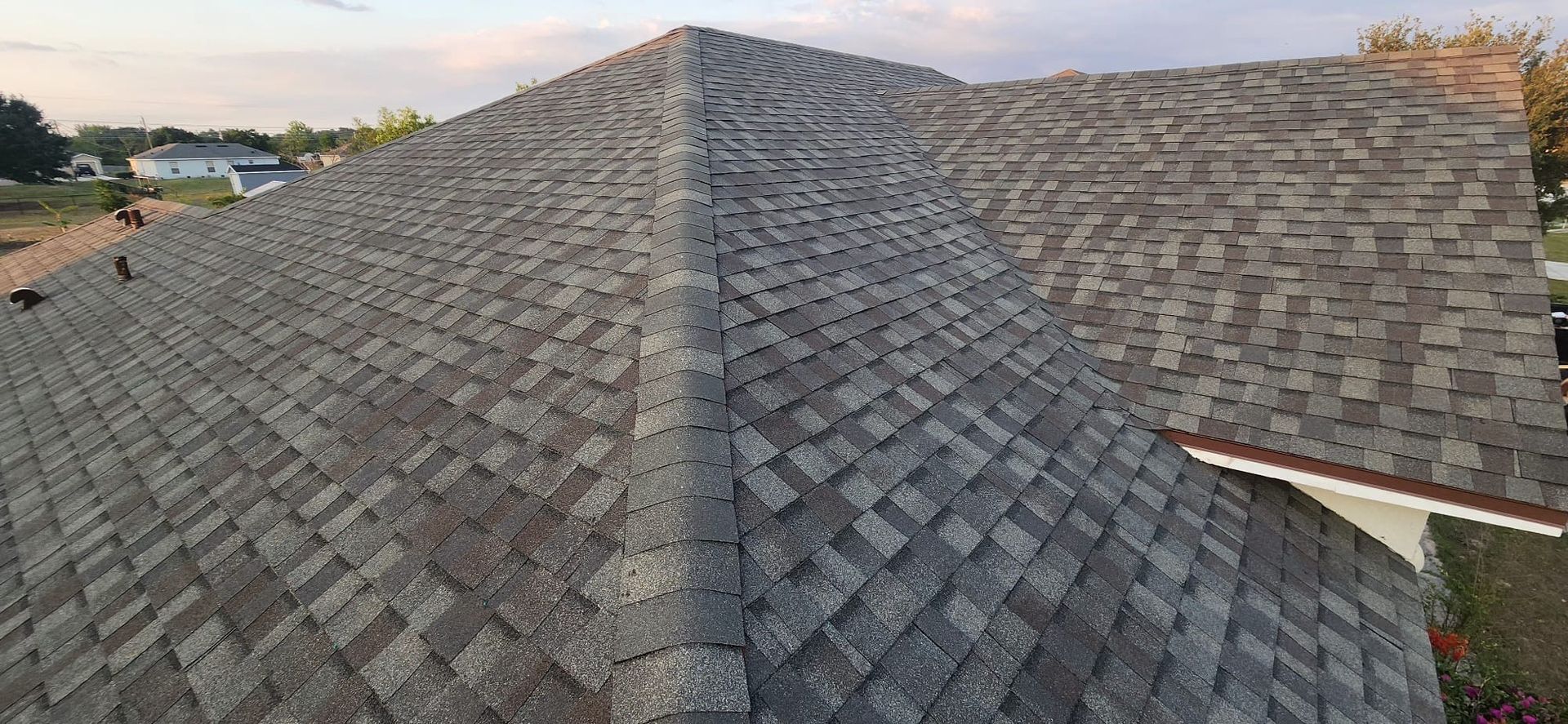Aerial view of a gray shingled roof with a ridge line at sunset