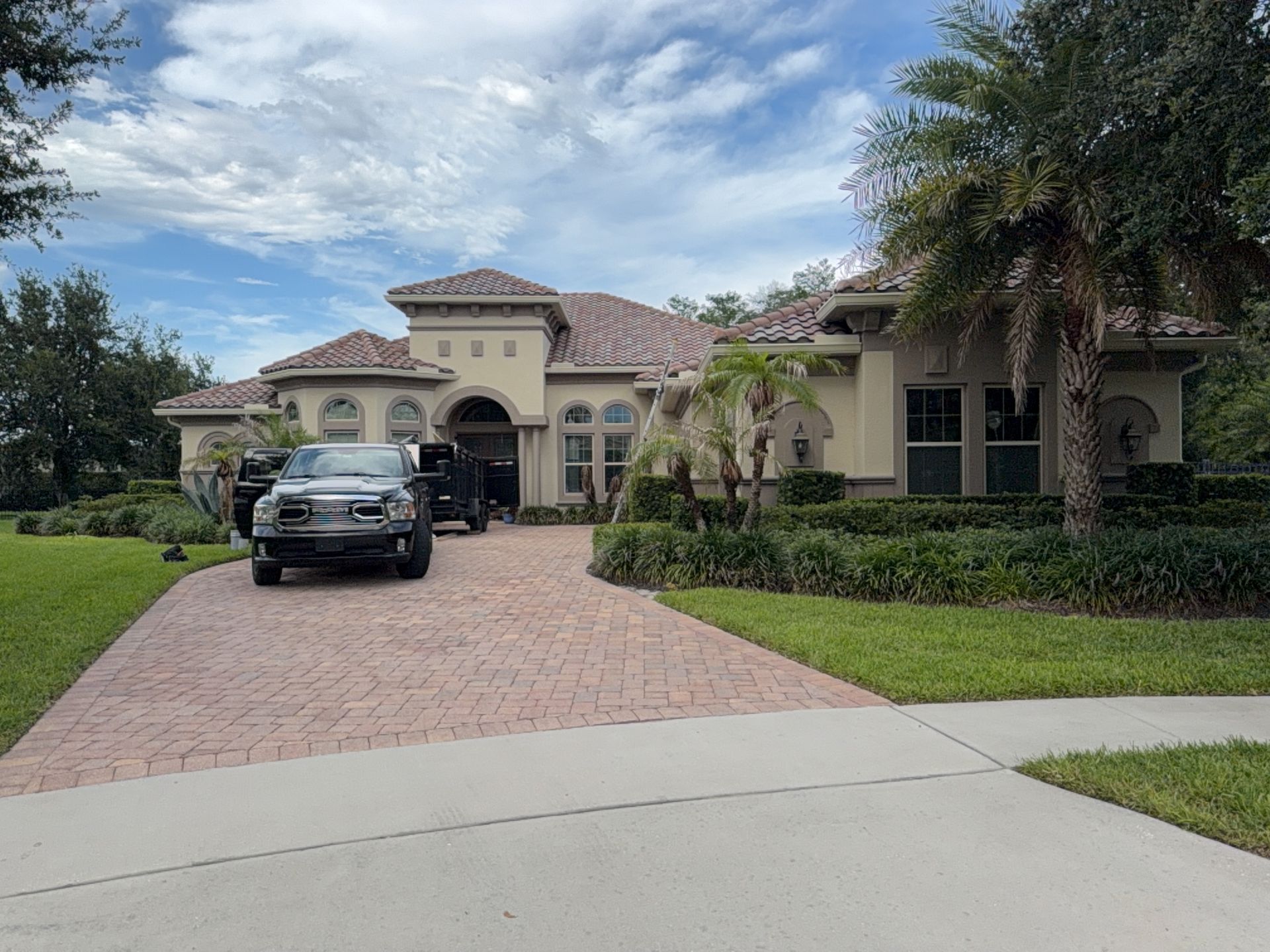 Luxury stucco house with a black SUV parked in the brick driveway on a suburban street