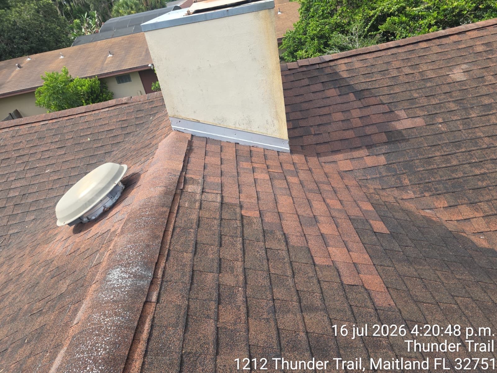 Rooftop with brown shingle roof, white chimney, and round vent cap under a clear sky.