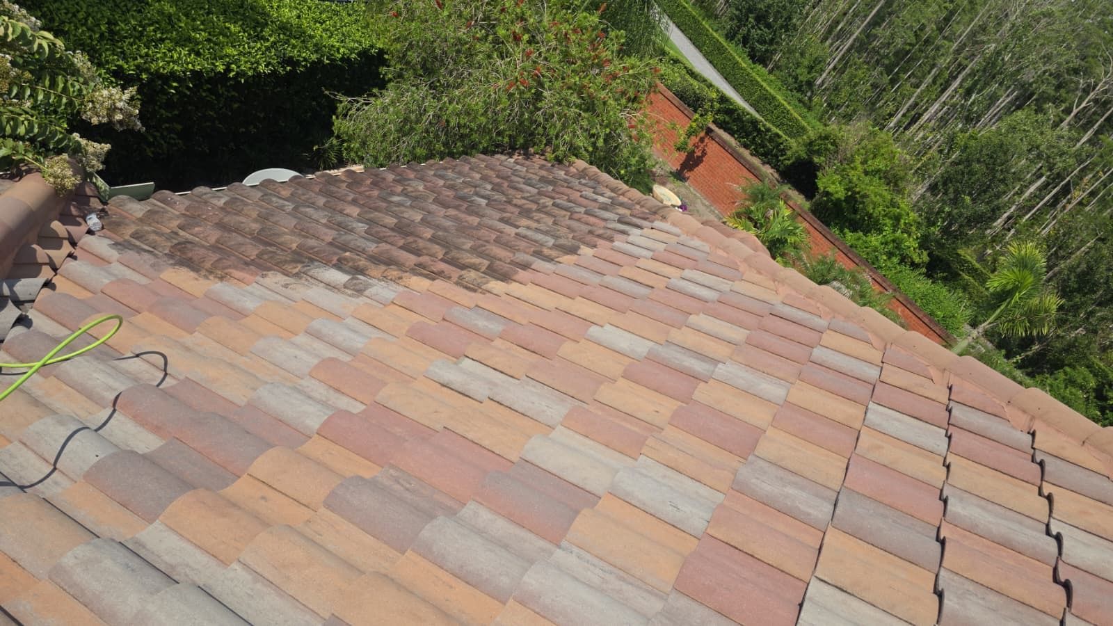 Tilted view of a tiled rooftop bordered by green trees and a red brick wall