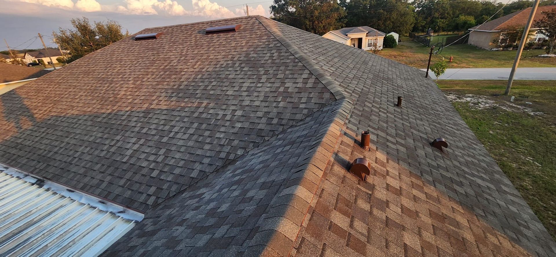 Aerial view of a shingled roof with several dark stains and a rooftop vent near a street