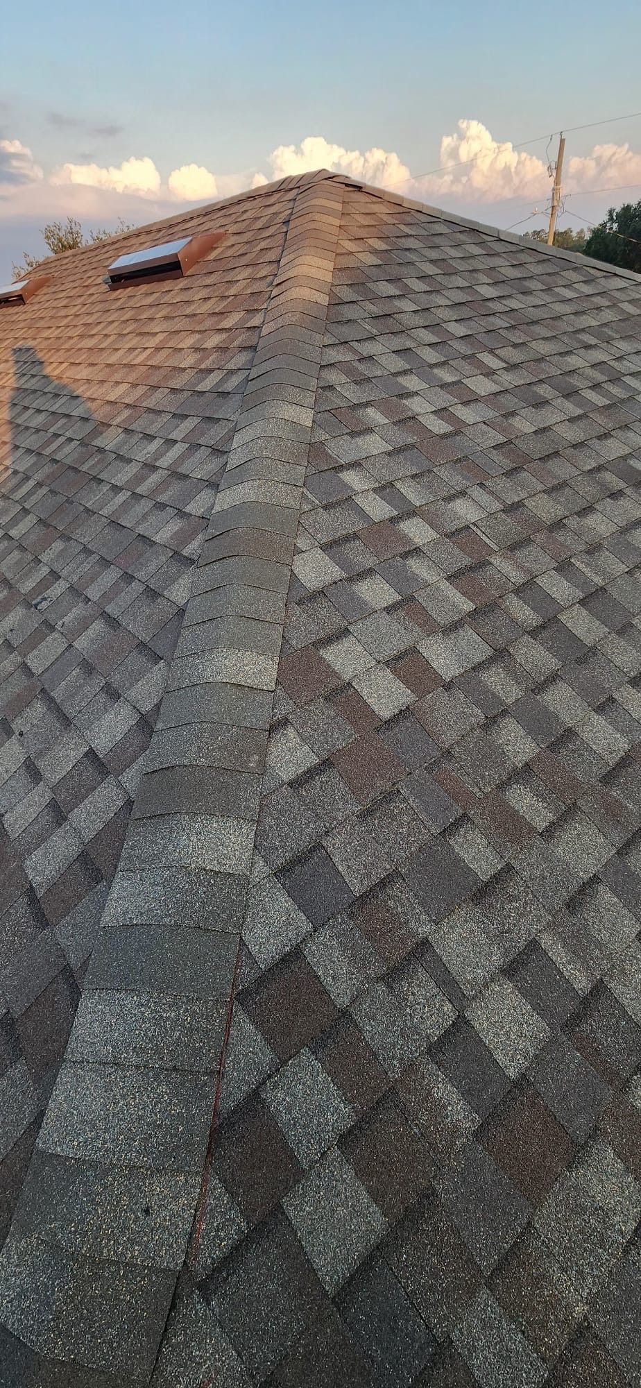 Gray shingled roof ridge at sunset with a small roof vent and clouds in the sky
